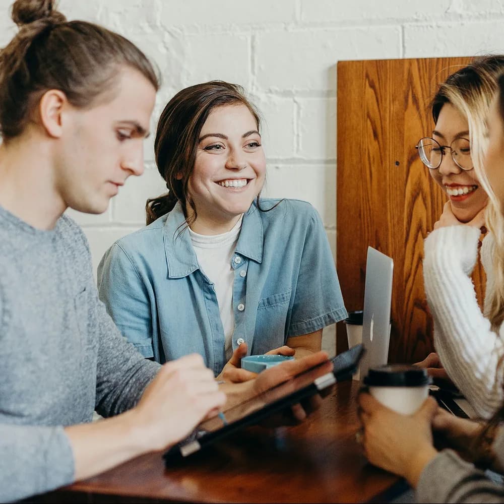 Quatre collègues en discussion autour d'une table, souriants.
