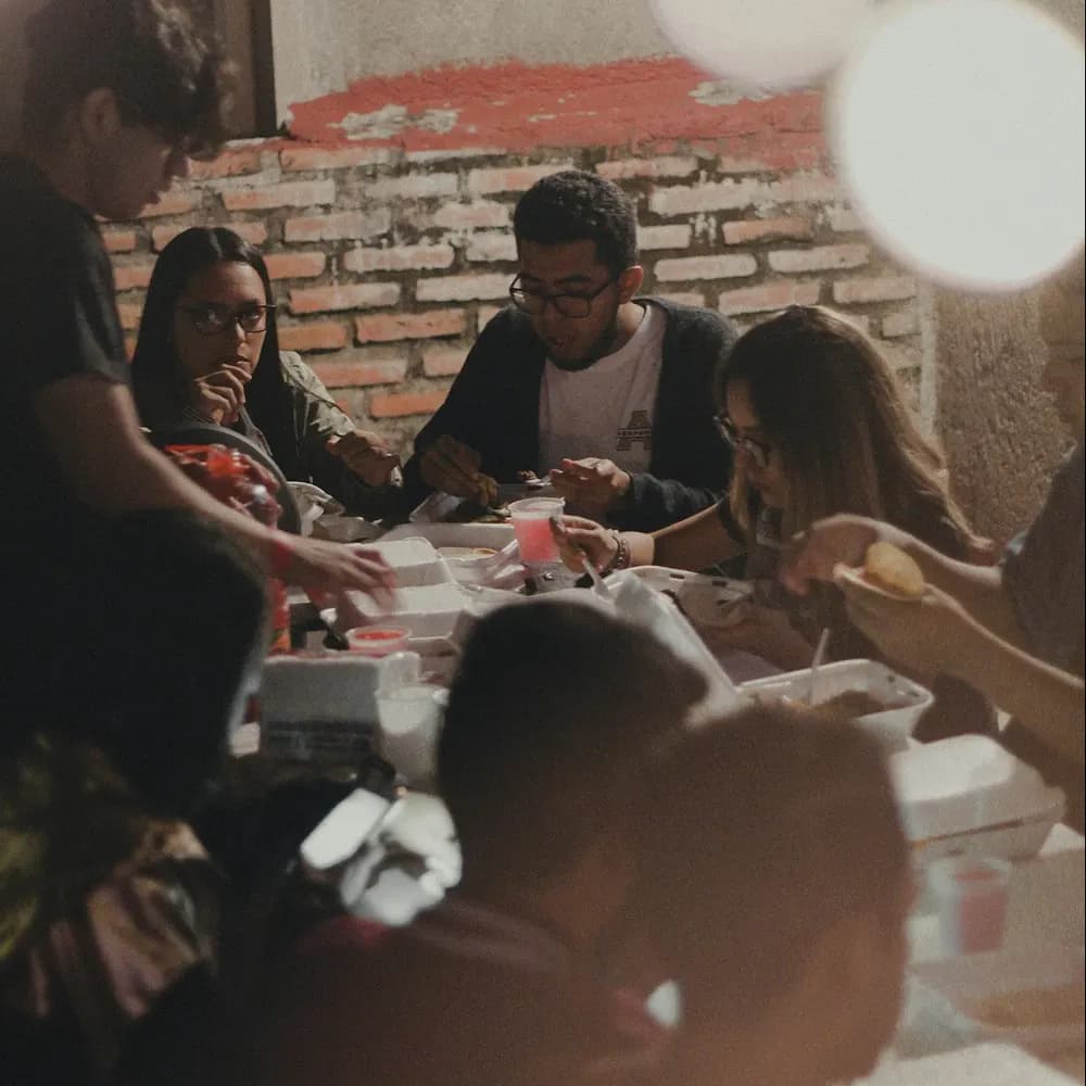 Un groupe attablé partage un repas sous des lampes rondes, dans une salle aux murs de brique.